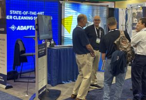 four men in front of a blue booth at a tradeshow talking