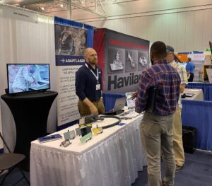 A laser cleaning sales man stands at a white curtained table and talks to two visitors